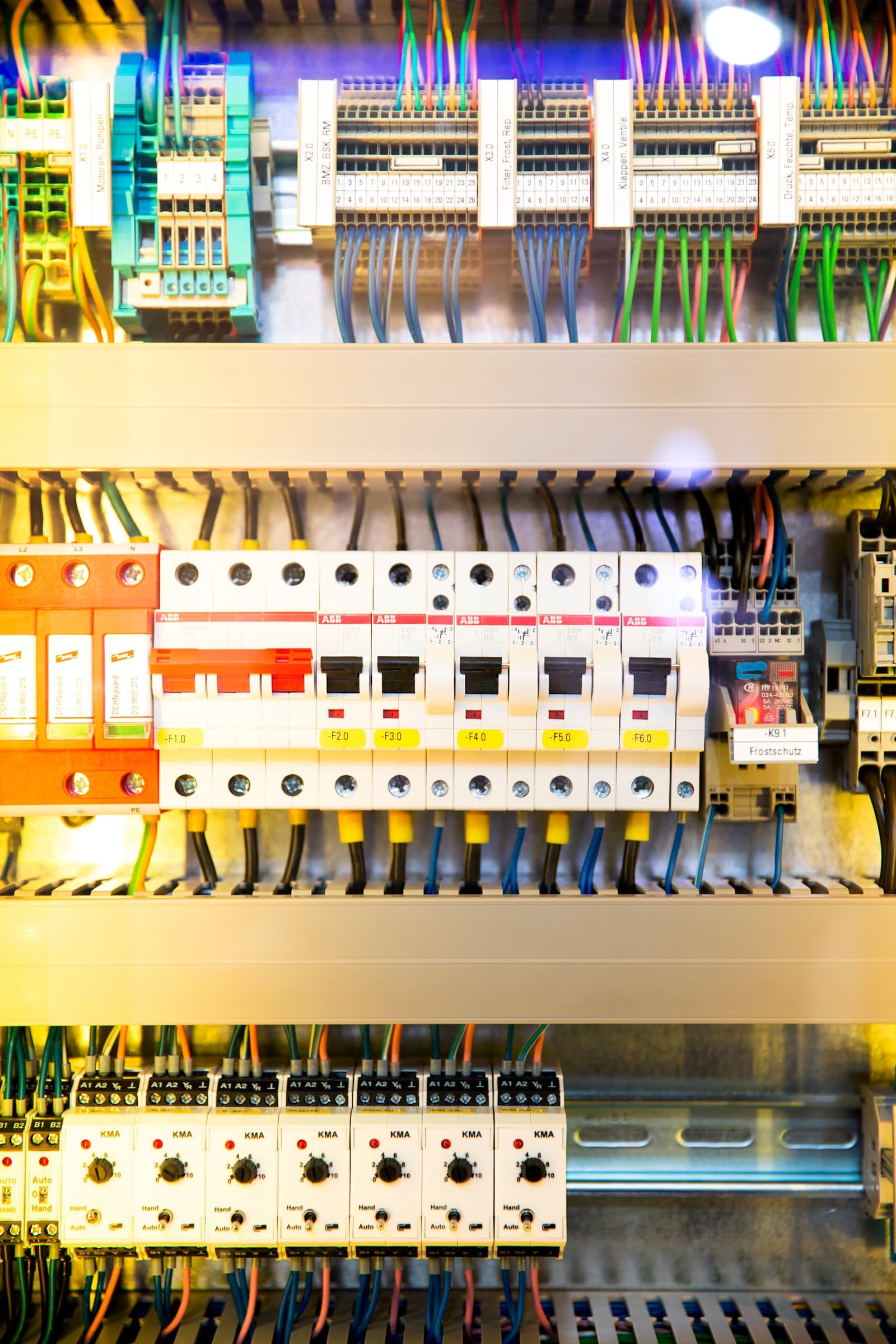 The inside of an industrial control cabinet: DIN-rail circuit breakers, relays and colour-coded field wiring