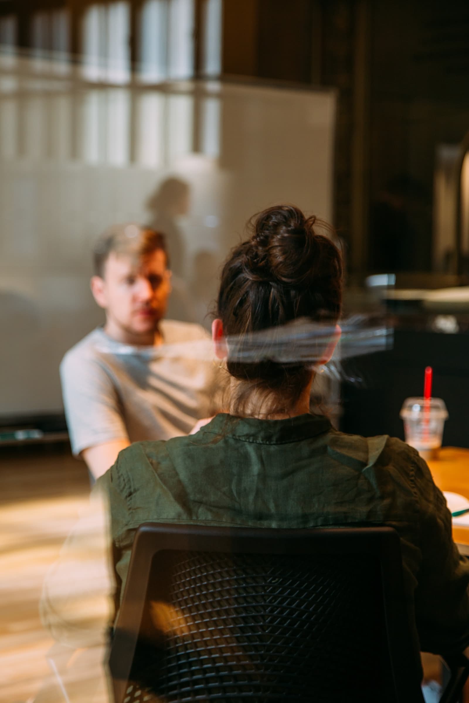 Two colleagues talking across a table, seen through a glass partition
